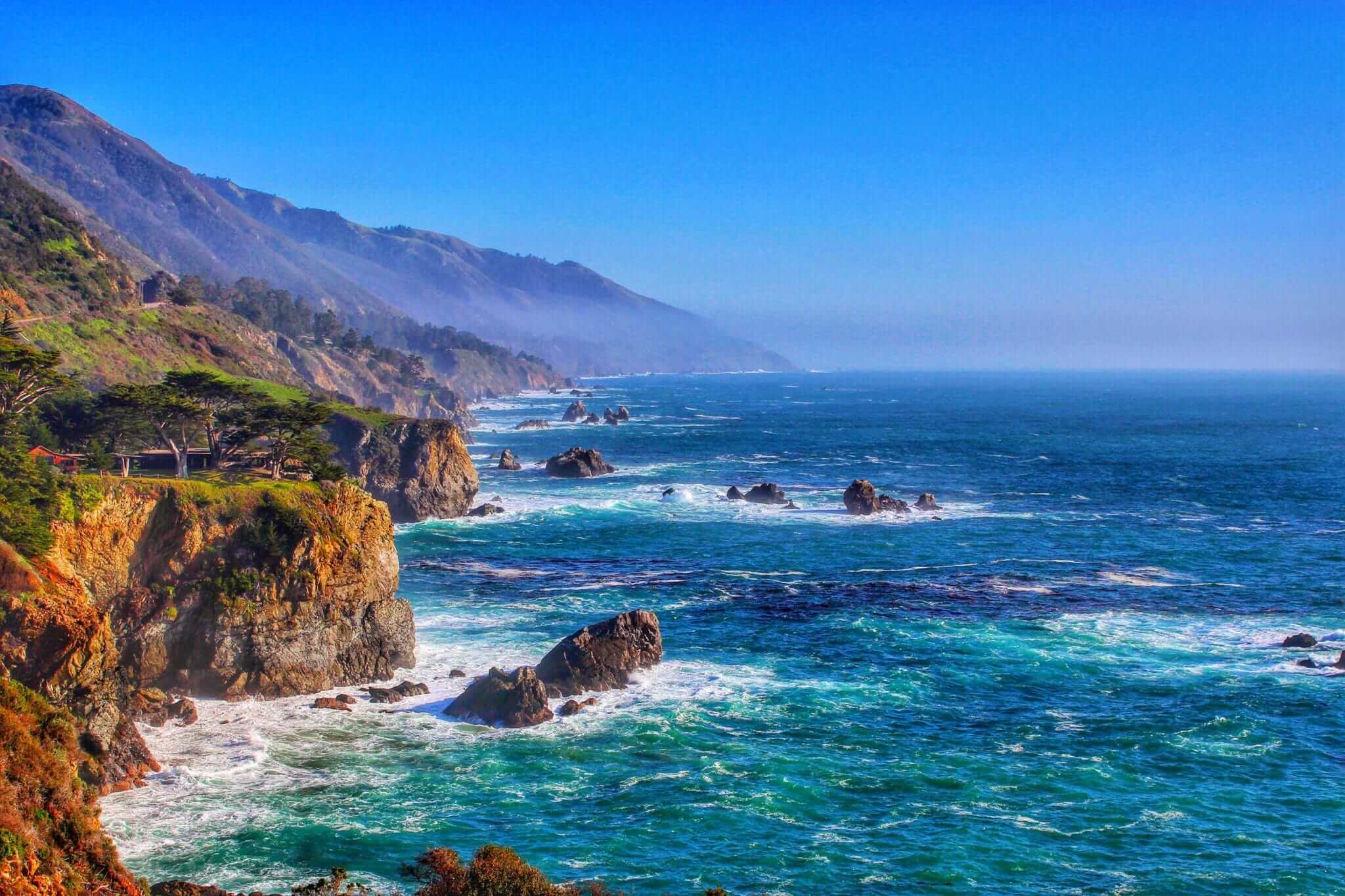 Coastal view of Big Sur with mountains and deep blue ocean crashing against the cliffs