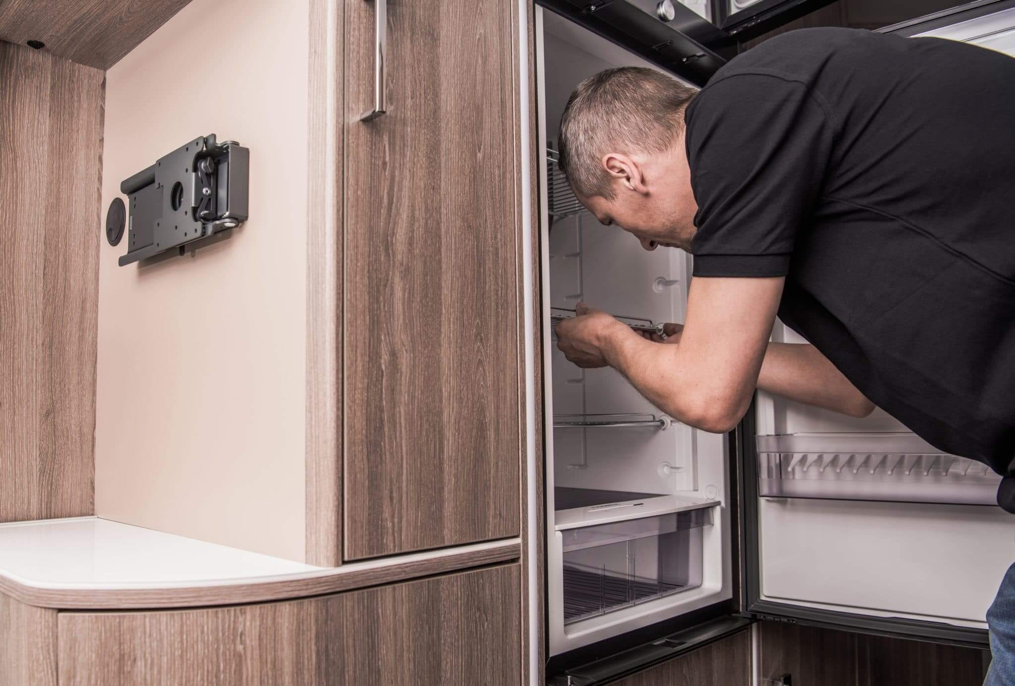 Man bending over doing a RV refrigerator repair