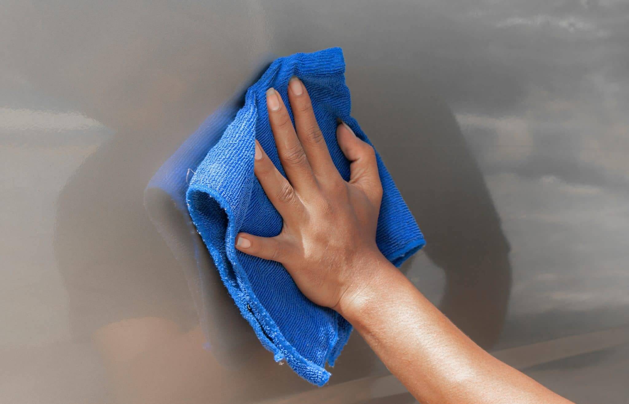 A hand is holding a blue microfiber cloth while waxing an RV with the best RV wash and wax.