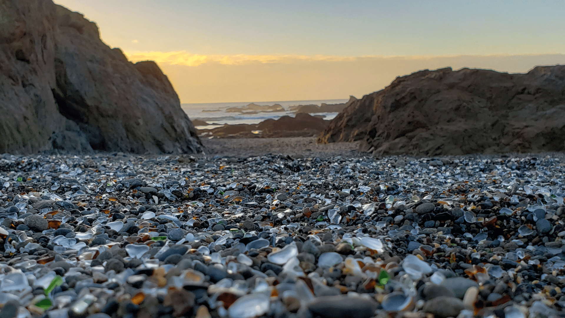 Sea glass on the beach in the forefront and cliffs and the ocean at sunset in the background in Fort Bragg,CA.