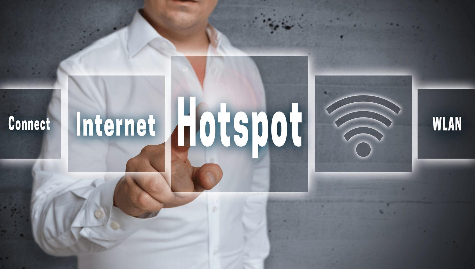 A business man stands behind a clear board with the word hotspot in the middle which he is pointing to. It has other boxes stating internet, WLAN and connect and also has the wifi bar signal indicator.
