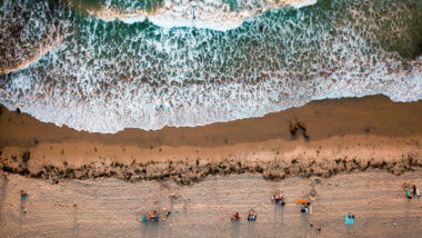 An overhead view of waves crashing on the shore with people sitting on the beach in San Diego which is a great place to beach camp in southern california.