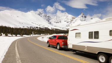 A red truck tows a travel trailer along a highway surrounded by snow and headed towards the snowy mountains! What is the best truck to tow a travel trailer?
