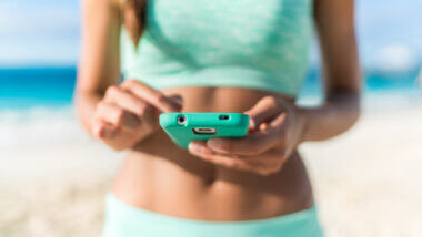 A woman in teal uses her phone to access 17 of the best RV apps suggested by Getaway Couple!