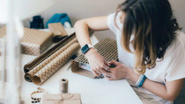 A woman wraps a personalized camping gift in tan paper wrapping.