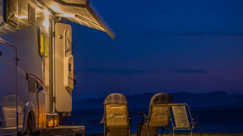 A dark blue night is lit up outside of an RV by the awning lights.
