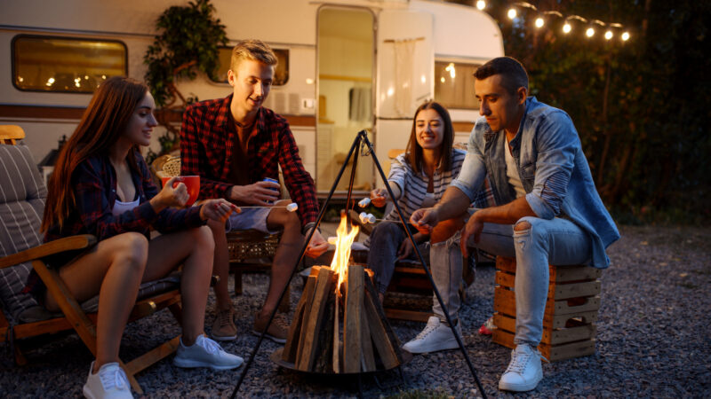 A group of young people enjoy campfire games and smores outside their RV.