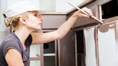 A woman paints a cabinet brown with a paintbrush.