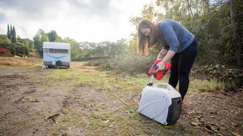 A woman puts fuel into her portable generator that powers her travel trailer.