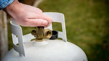 A hand reaches to refill an RV propane tank.