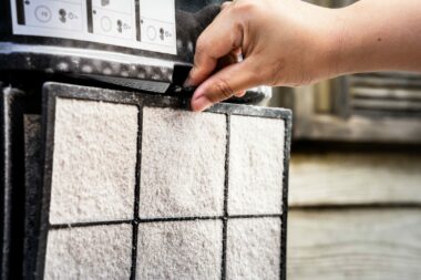 A hand removes a dirty air filter to clean and replace