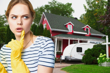 A woman with a questioning look wearing cleaning gloves in front of a red home with a travel trailer out front.