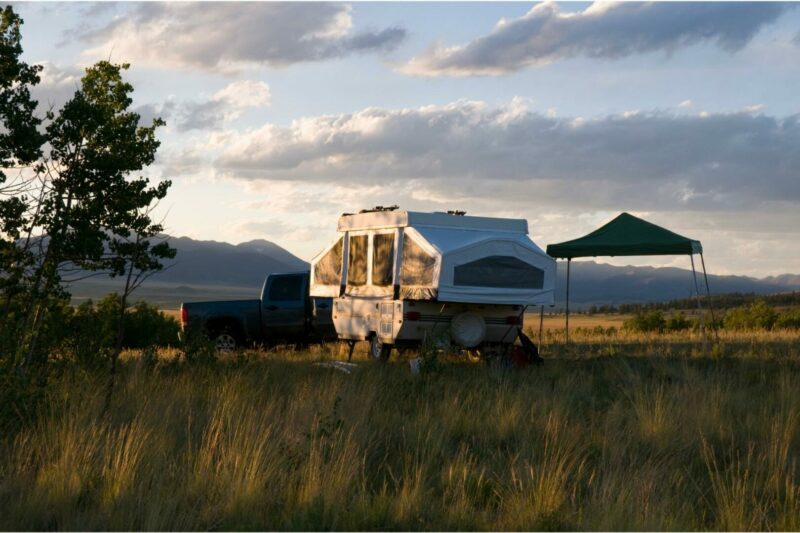 A pop-up camper camps out in a field next to its tow vehicle and canopy