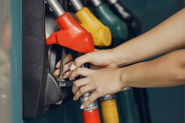 Hands reach and grab one of four fuel pumps at a gas station