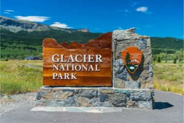 A sign outside of Glacier National Park made of wood and stone and sporting the National Park Service logo.