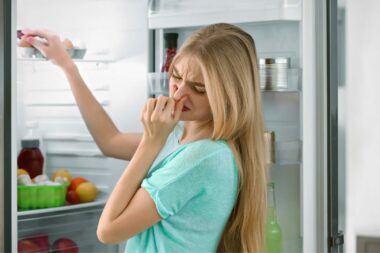 A woman holds her nose to keep from smelling spoiled food as she finds her refrigerator has stopped working.