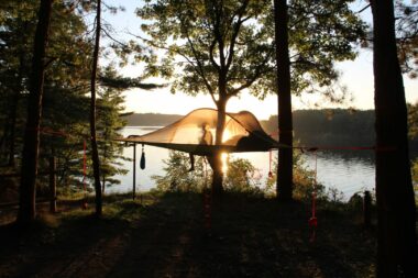 A hammock glows between two trees camping on the water in Michigan.