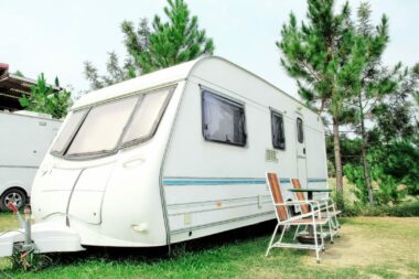 A travel trailer parked at a campground with chairs set up out front in the green grass.