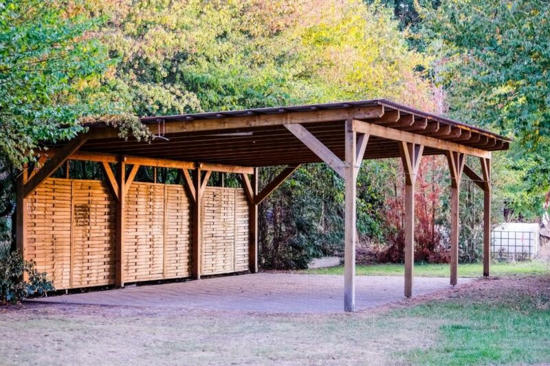 A wooden carport with a concrete pad big enough for a small RV to be stored.