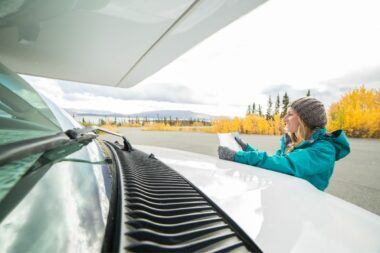 A woman leans on the hood of an RV as she studies her road trip map.