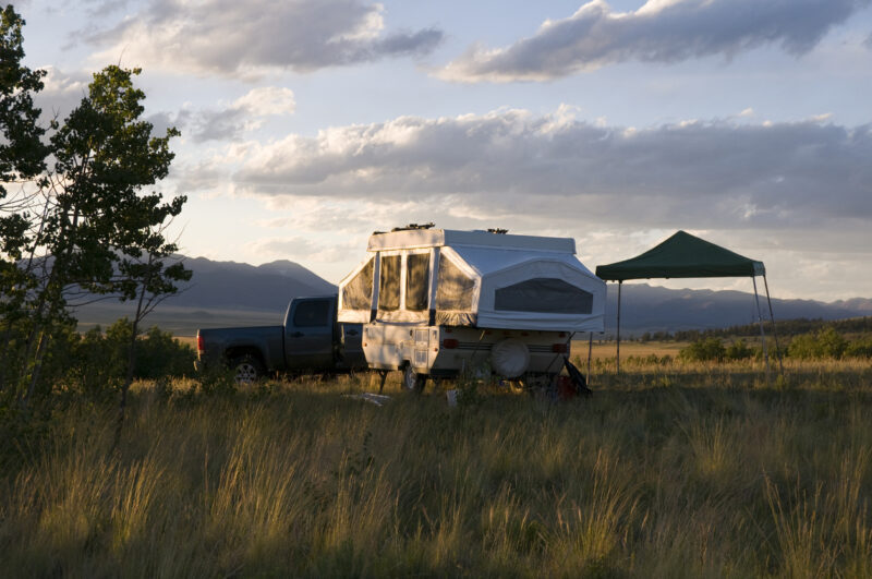 A small pop-up camper sitting in a meadow before the owner puts hard sides on their pop-up camper.