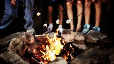 A group roasting marshmallows around a campfire at night that was started by following five rules for the perfect campfire