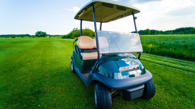 A golf cart on the green with a fan