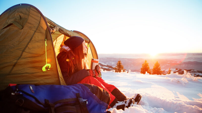 A woman sitting outside of her tent in the snow using a tent heater