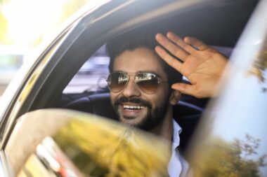 A celebrity waves out the window of a vehicle.