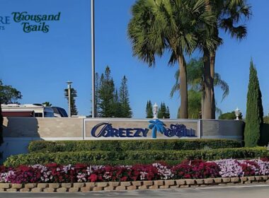 The Breezy Hill Sign with flowers blooming below it and a bright blue sky above it.