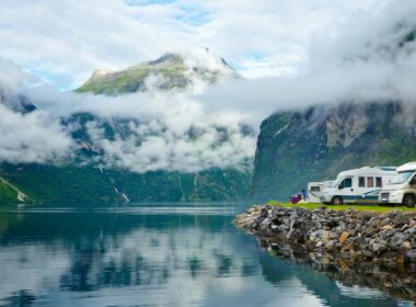 A row of motorhomes parked along an embankment of a turqoise lake and mountain range.