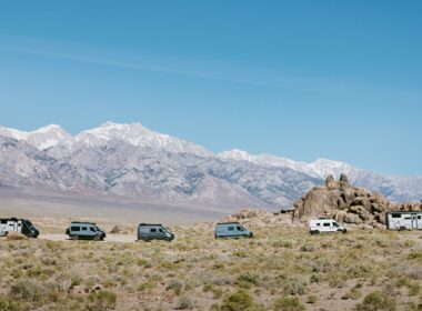 A lineup of six Winnebago travel vans in front of a mountain range.