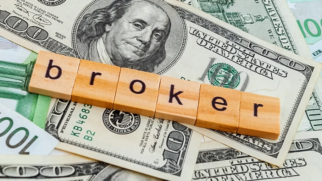 A stack of money with the word "broker" spelled out with Scrabble tiles.