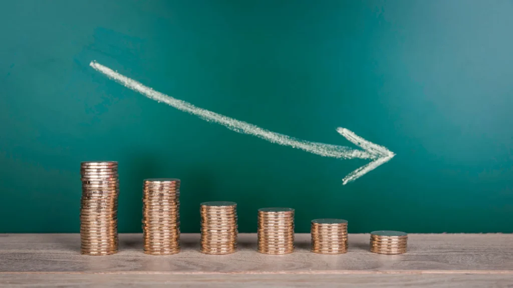 A downward arrow drawn on a chalkboard as coins are stacked beneath in five stacks, decreasing in height.