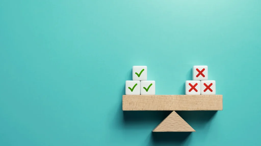 Block set up balanced with cubes containing green checkmarks on the left equal to the cubes with red x's on the right as it sits against a teal background.