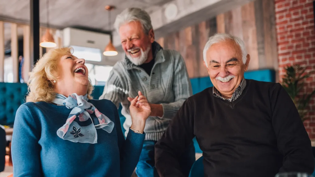 Three senior people laughing together in what seems like a restuaruant.