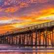 Boardwalk dock in Flagler Beach Florida at sunset with an orange and blue sky painted with orange, pink, and purple clouds.