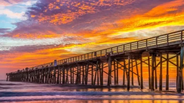 Boardwalk dock in Flagler Beach Florida at sunset with an orange and blue sky painted with orange, pink, and purple clouds.