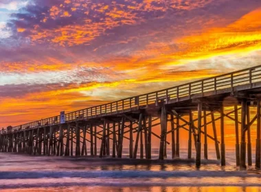 Boardwalk dock in Flagler Beach Florida at sunset with an orange and blue sky painted with orange, pink, and purple clouds.