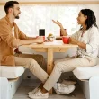 A couple seated in their dinette within their RV as they look at each other and talk, while drinking coffee out of red mugs.