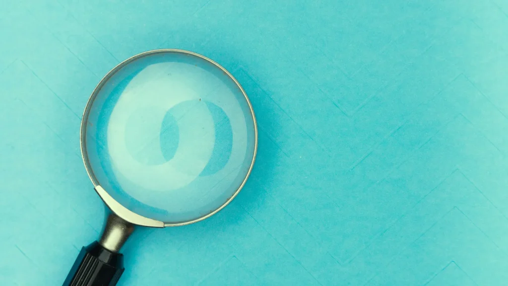 A teal blue background with a partial view of a mangifying glass against it.