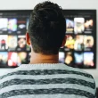 A person looking at their mounted TV on the wall, presumeably looking for something to watch as they sit seated.