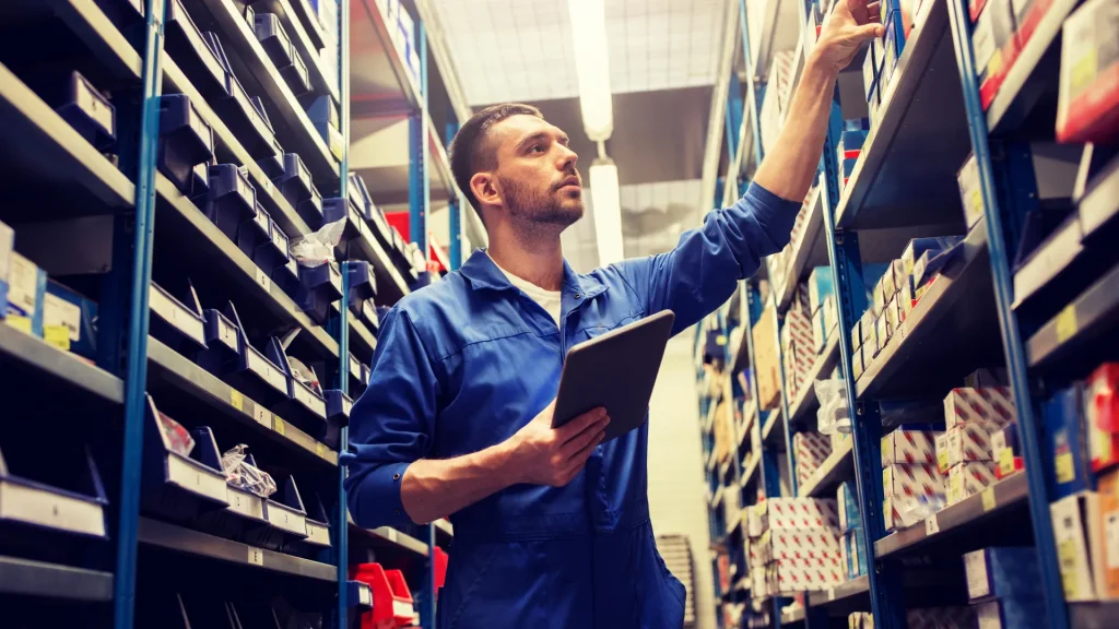 A person in a parts store in a blue jumpsuit with a tablet in their hand as they look for a part.