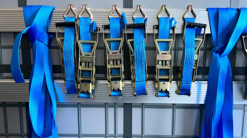 A row of blue ratchet straps in varying sizes hung around metal shelving as to keep them organized.