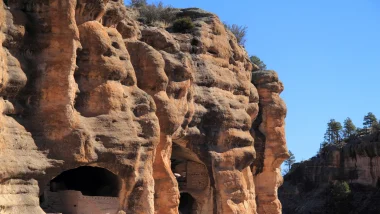 Gila Cliff Dwellings National Monument in New Mexico. This photo showcases the dwellings within the rust-colored cliff face as it contrasts the clear blue sky in the background.