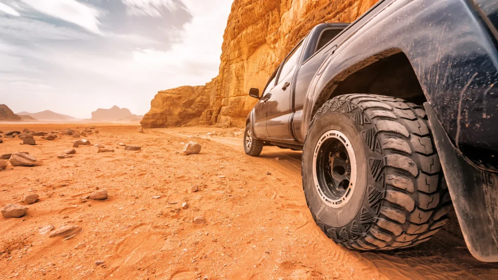 An up-close photo of a black four-wheel drive pick-up truck in a desert landscape, contrasted by the bright orange rocks and sand.