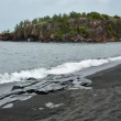 Black Beach in Minnesota. The day is overcast as the water washes up onto the black beach. An island sits in the distance.