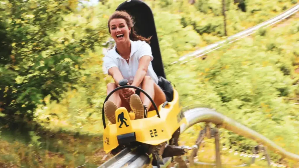 A woman riding the Rail Runner Mountain Coaster at Anakeesta. She's smiling as the yellow coaster rushes on.