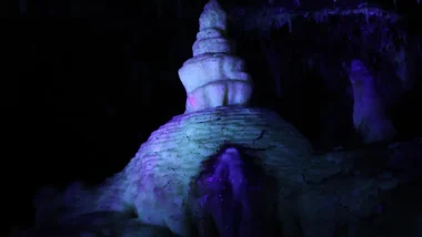 A formation within the Crystal Lake Cave during their blacklight tour as purple, blue, and teal light pools onto the formation in the dark cave.