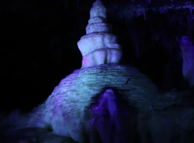 A formation within the Crystal Lake Cave during their blacklight tour as purple, blue, and teal light pools onto the formation in the dark cave.